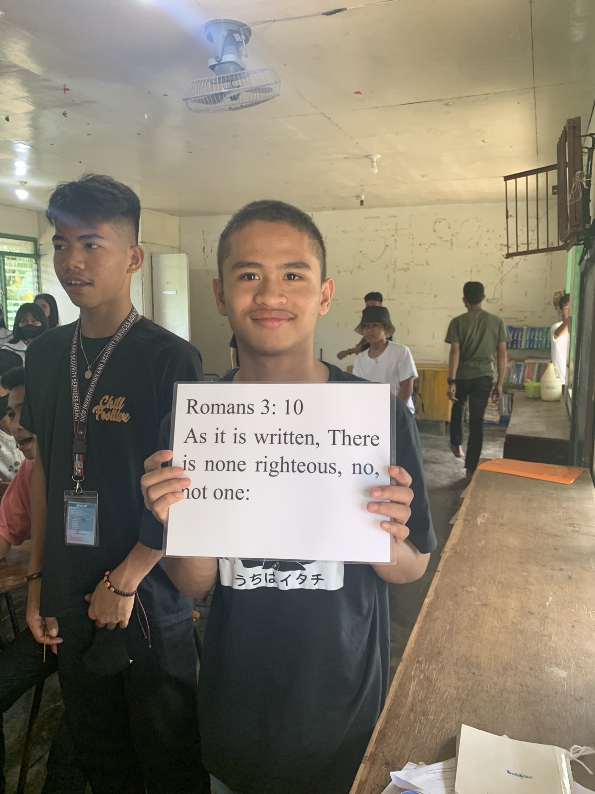 A young Filipino male high school student holding a Romans 3:10 verse card during a classroom evangelism visit